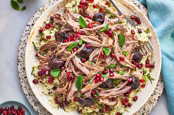 Plate of shredded leg of lamb topped with prunes, pomegranate seeds and mint