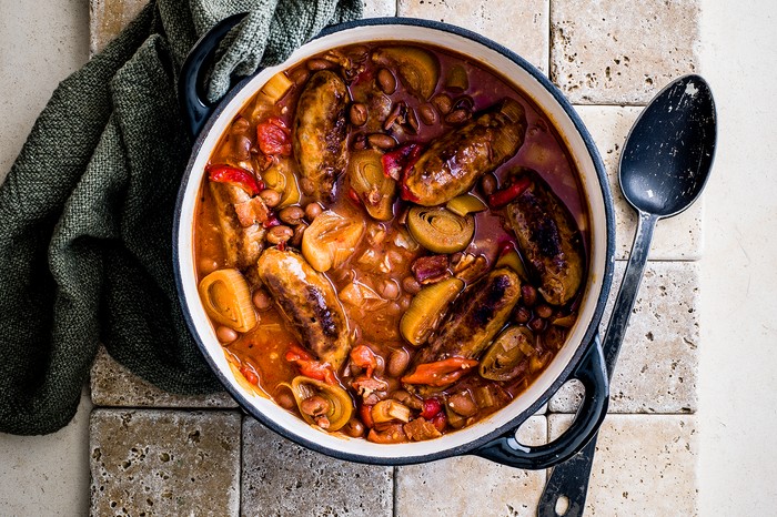 Pot of sausage casserole next to a tea towel and spoon