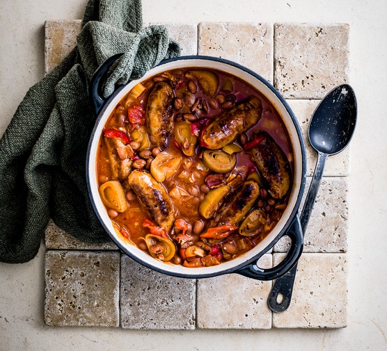 Pot of sausage casserole next to a tea towel and spoon