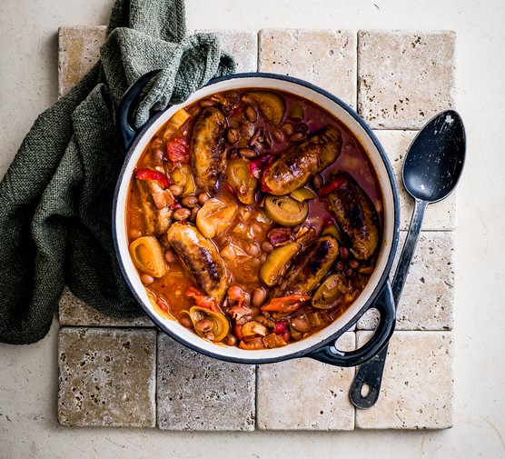 Slow Cooker Sausage Casserole Recipe Pot of sausage casserole next to a tea towel and spoon
