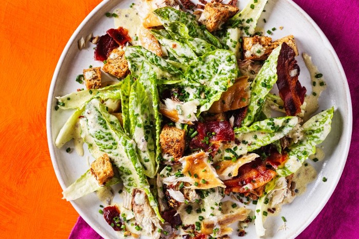 A white plate of lettuce, mackerel and croutons slicked in a creamy dressing