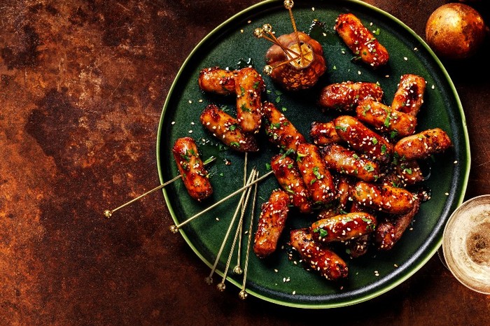 A green plate of cocktail sausages with cocktail sticks on a mottled brown background