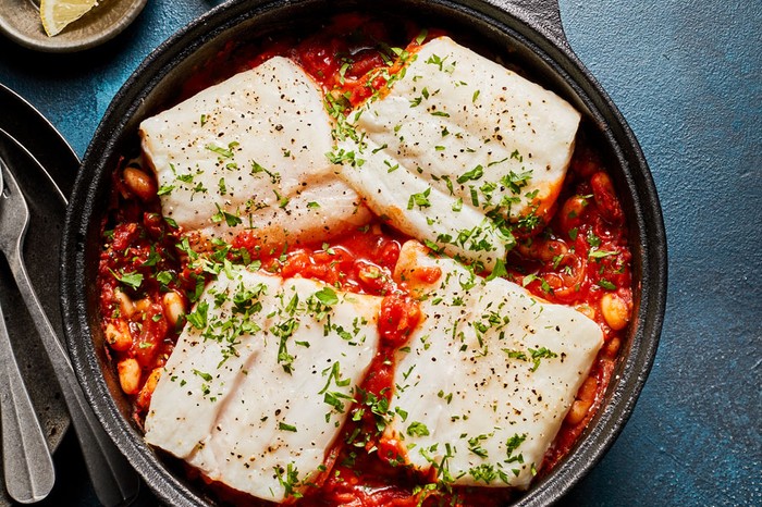 Pot of cod fillets in a tomato and bean sauce topped with parsley