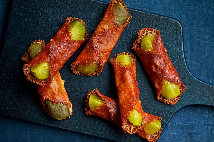 Board of cheese wrapped pickles next to a dip