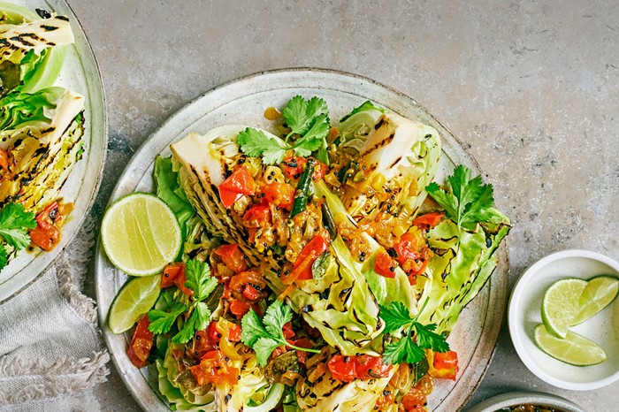 Plate of grilled cabbage topped with tomatoes and onions, next to lime lime slices.