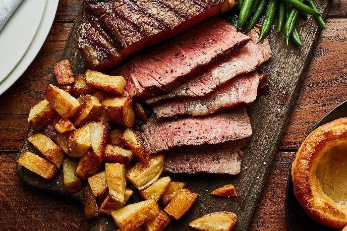 A wooden board filled with a sliced steak and thick cut chips