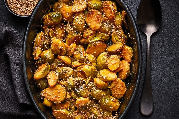 An oval oven dish filled with miso roasted sprouts on a black background