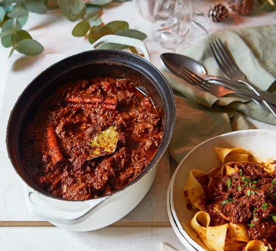 An ovenproof pot filled with stifado stew, next to a bowl of pasta with the stew piled on top