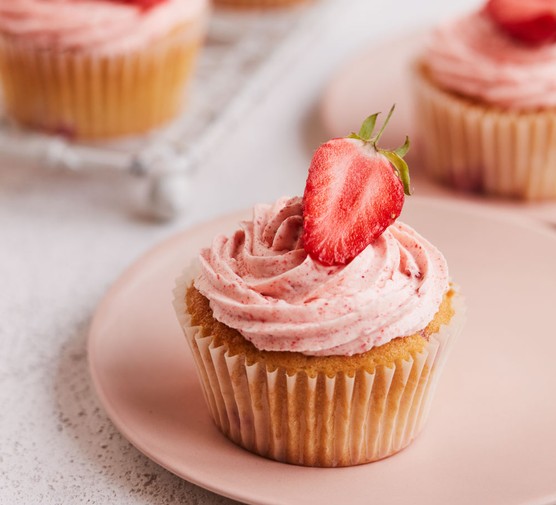 Strawberry cupcakes topped with pink frosting and a strawberry half