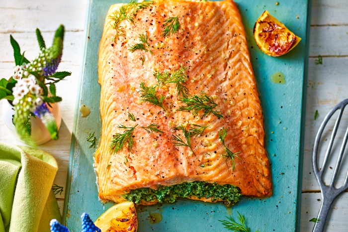 salmon stuffed with a green herby mixture and topped with dill fronds on a blue chopping board with a green napkin