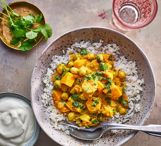 Bowl of sweet potato and chickpea curry on a bed of rice sprinkled with coriander, next to a bowl of yoghurt