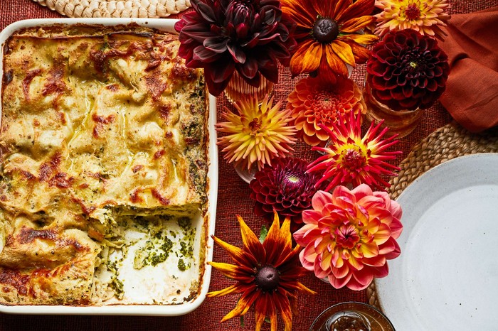 A whole lasagne with a serving on a side plate