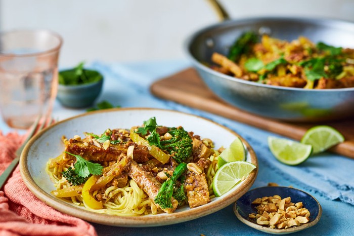 Plate of tempeh stir-fry in focus with pan of it behind out of focus