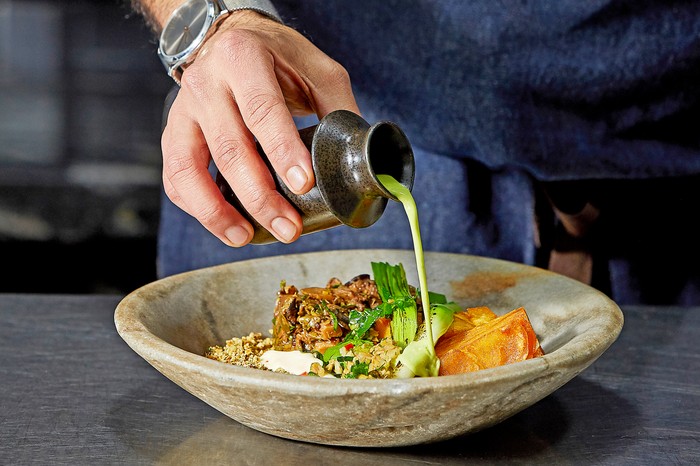 Tendril A man pouring a sauce over a dish at Tendril, which showcases a mostly vegan menu