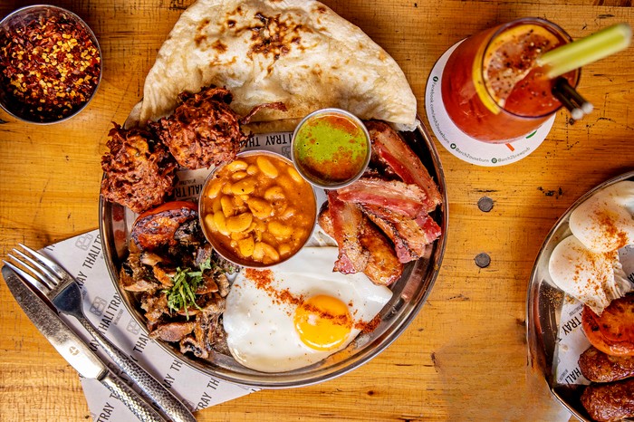 A metal tray loaded with regional curries, fresh naan, puri, cardamom lemon rice and pickles