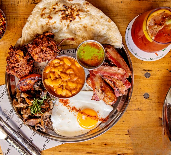 A metal tray loaded with regional curries, fresh naan, puri, cardamom lemon rice and pickles