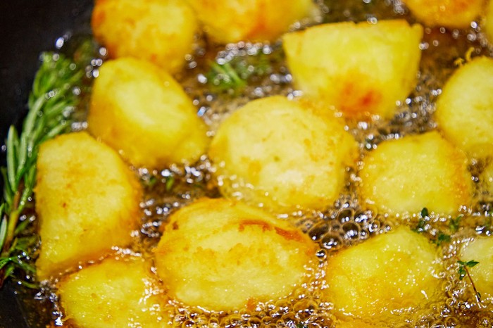 Potatoes roasting in fat in a tin with thyme on the side