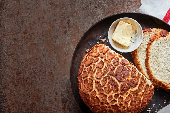 A crackled loaf of bread with slices taken out of it and butter on the side