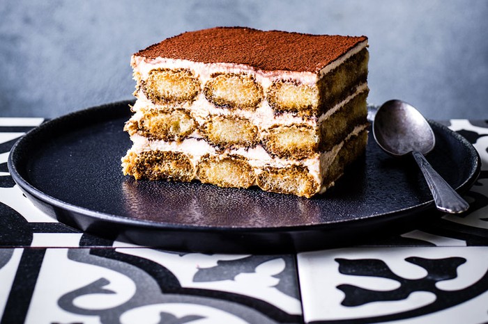 A large slice of tiramisu on a dark plate