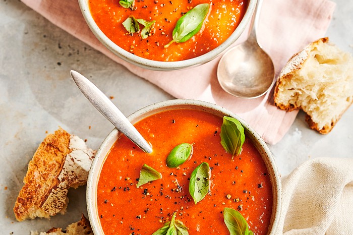 two bowls of red soup scattered with basil leaves and sat on folded linen napkins with chinks of crusty bread