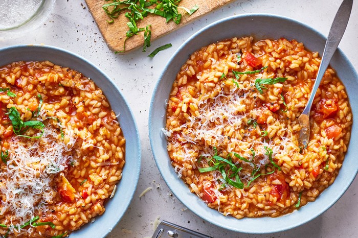 Two bowls of tomato risotto next to a chopping board with basil on top