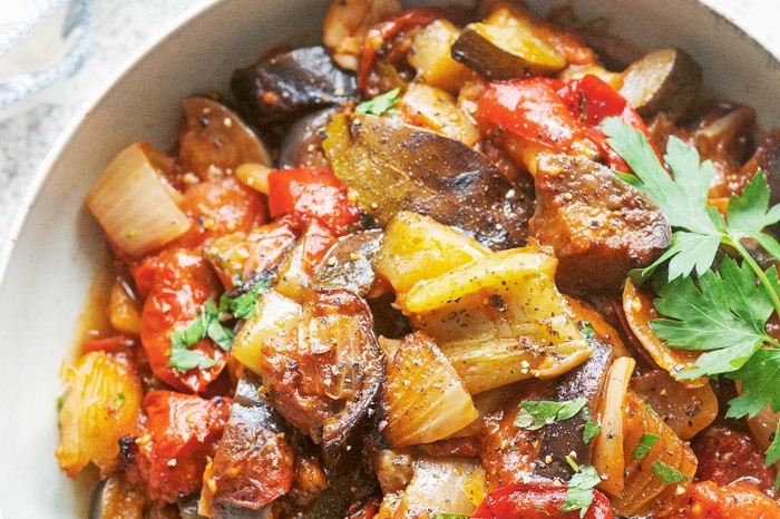 White bowl filled with roasted veg and green herbs on a marble background