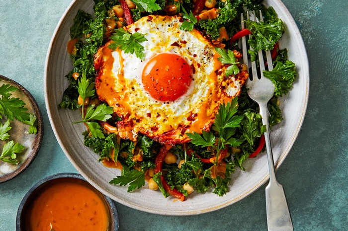 Plate of kale salad topped with a turmeric fried eggnext to a ramekin of dressing and parsley