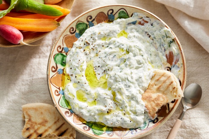 A bowl of tzatziki with a flatbread dipped in