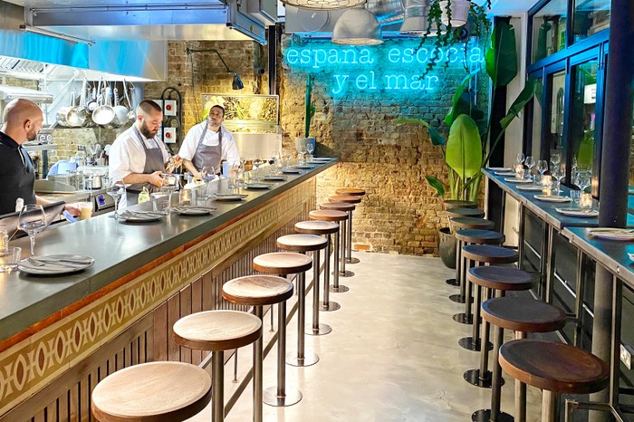 The interior at tapas restaurant Maresco, featuring a feature brick wall, a blue neon sign and exposed ventilation ducts