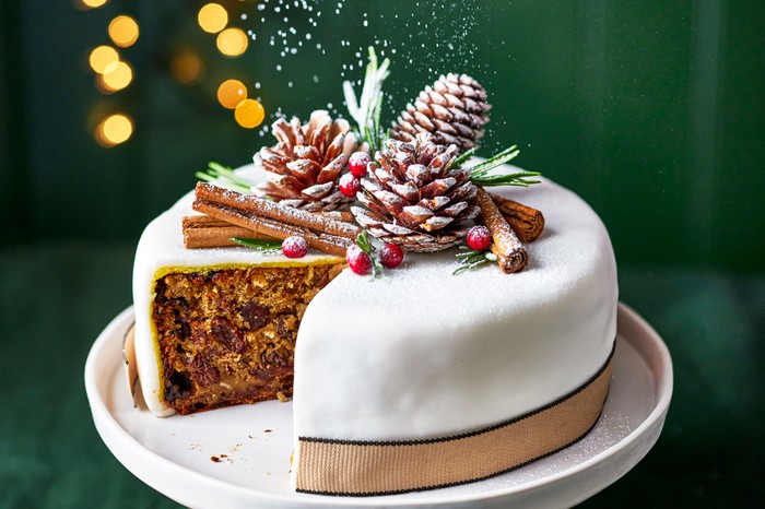 A vegan christmas cake with icing and decorations placed on a white cake stand