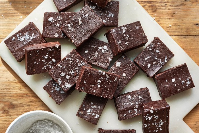 Squares of chocolate vegan fudge with topped with salt flakes on a white chopping board