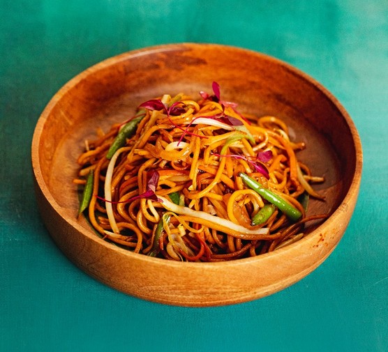 A wooden bowl filled with noodles and veg on a green background