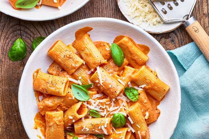 A plate of tomato penne pasta with a small plate of grated parmesan on the side