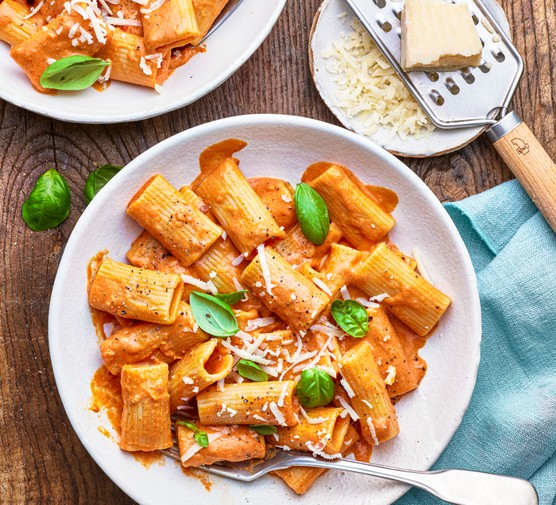 A plate of tomato penne pasta with a small plate of grated parmesan on the side