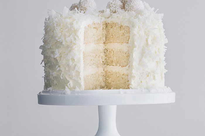 Layered sponge cake with centre showing, covered in cream cheese icing and coconut shavings