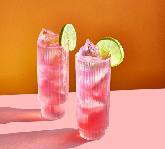 Two pink cocktails in tall glasses garnished with a slice of lime