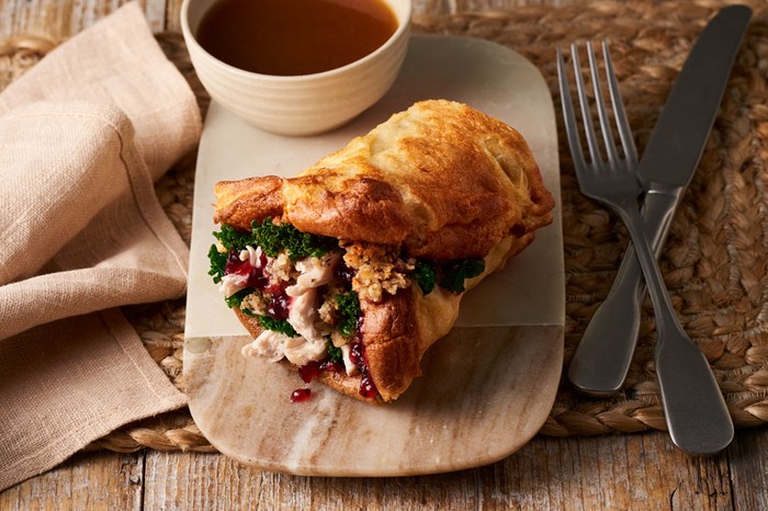 Chicken, kale and cranberry sauce wrapped in a yorkshire pudding next to a pot of gravy