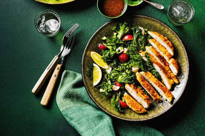 Green bowl with almond-crusted chicken and kale sumac salad with cutlery on the side