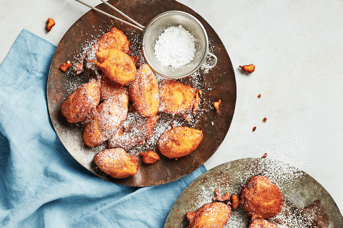 Plate of banana fritters on a white background with a blue napkin and mini sieve of icing sugar