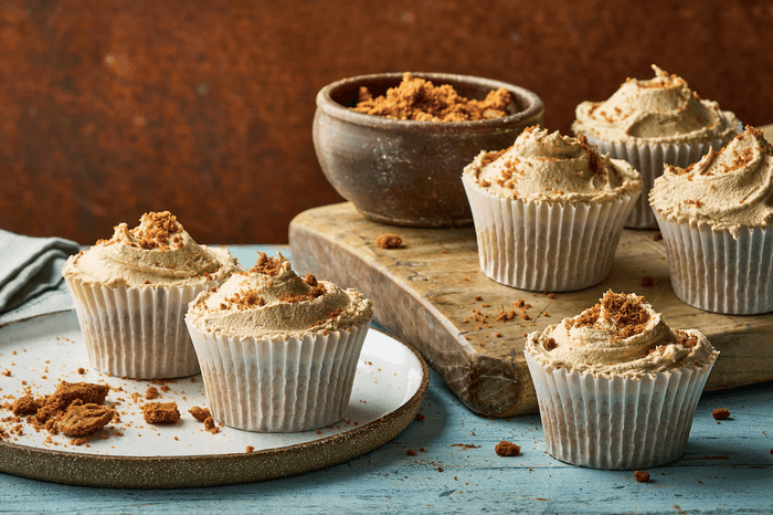 A wooden board and ceramic plate topped with cupcakes on a blue wooden surface