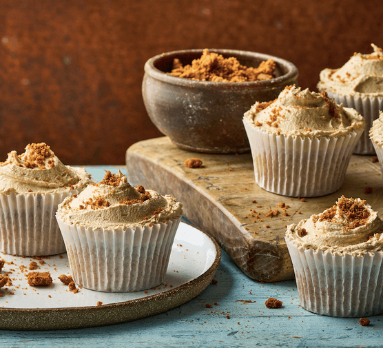 A wooden board and ceramic plate topped with cupcakes on a blue wooden surface