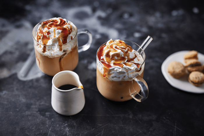 Caramel iced coffee Two glass mugs of coffee topped with whipped cream and caramel sauce, with a small white jug of caramel