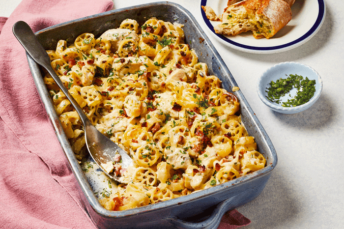 Chicken and bacon pasta bake in a dish with garlic bread on the side