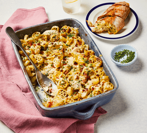 Chicken and bacon pasta bake in a dish with garlic bread on the side