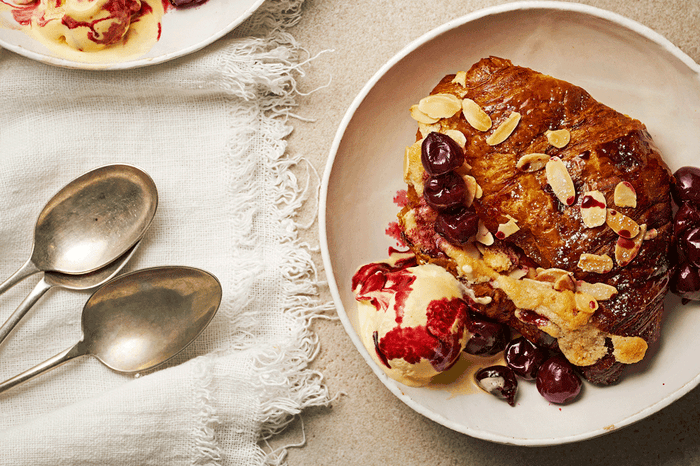 Croissant stuffed with cherries and sprinkled with flaked almonds on a plate with a scoop of vanilla ice-cream