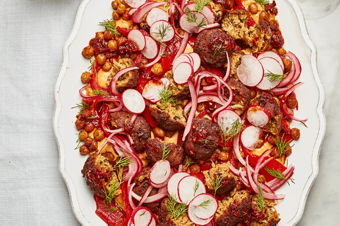 Smashed falafel with chickpeas, hummus and pink pickled onions on a white serving platter