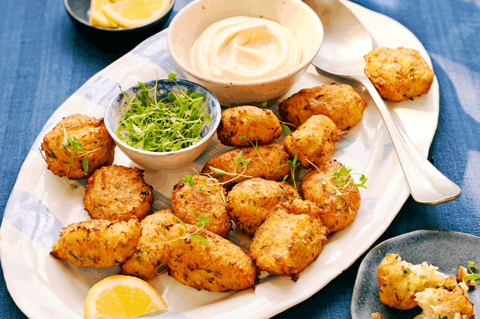 Bacalhau fritters on a plate with garlic mayo, lemon wedges and fresh herbs in a bowl