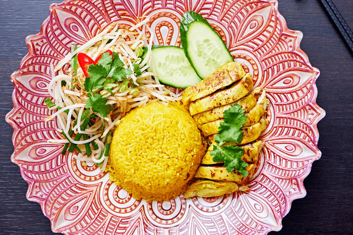 Decorated red plate topped with Hainan Malaysian chicken and rice dish with fresh cucumber slices