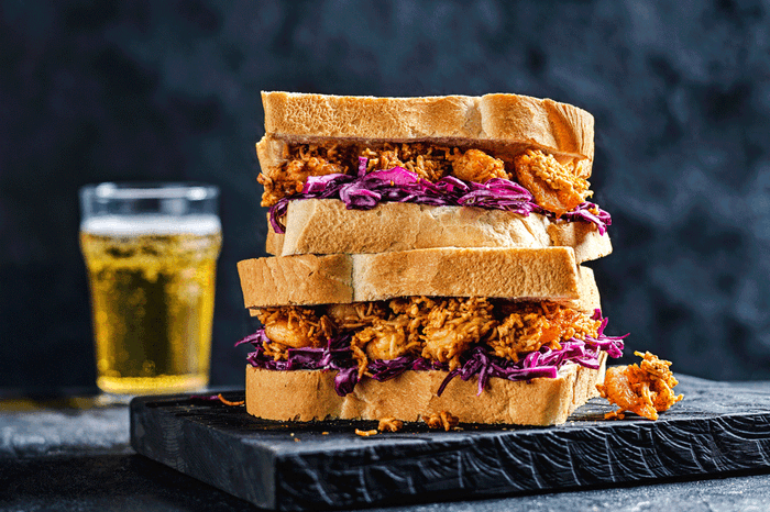 Po'boy prawn and instant ramen sandwich on a black slate with a glass of beer behind it