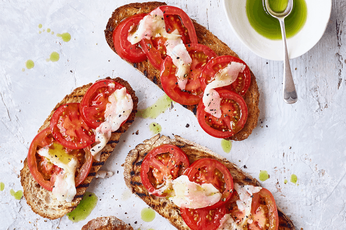 Slices of toasted bread topped with sliced tomatoes, slices of lardo and basil oil